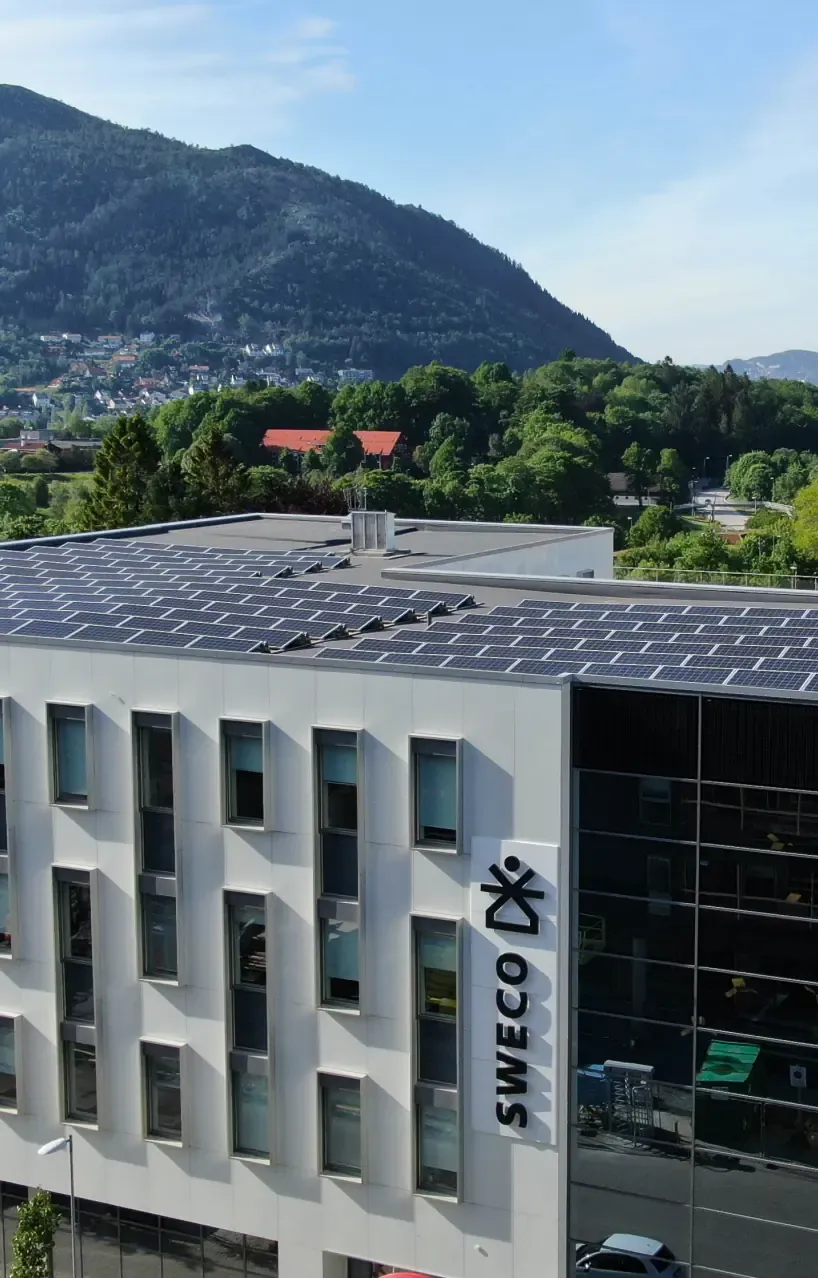Kontorbygg med solcellepaneler på det flate taket og en skogkledd ås bak